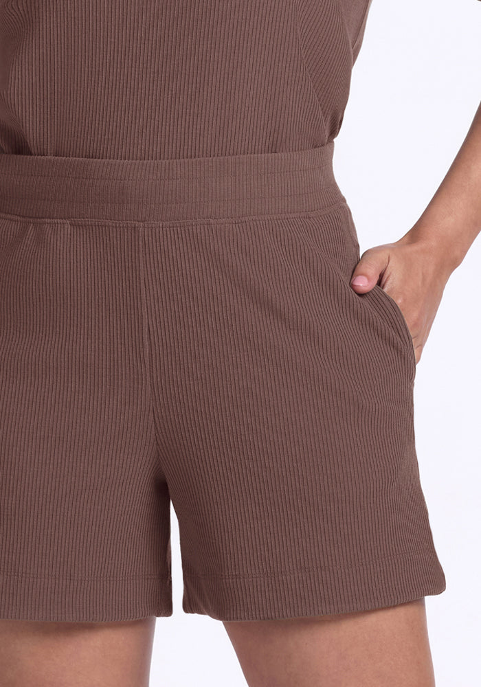A person wears Woolx Maisey Ribbed Shorts in Peppercorn with one hand in the pocket, shown waist to mid-thigh.