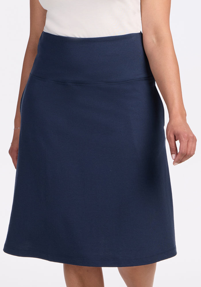 A person in a white top and the Woolx Marilyn Flowy Midi Skirt in Deep Navy stands with one arm relaxed by their side against a plain background.