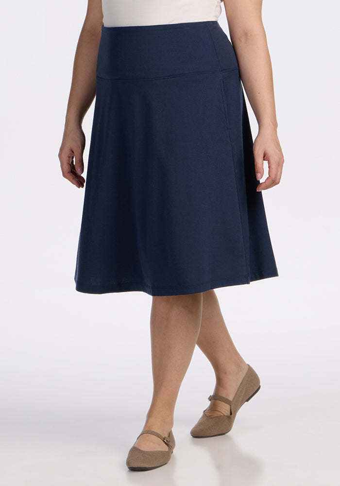 A person wearing the Woolx Marilyn Flowy Midi Skirt in Deep Navy, paired with a white top and tan flats, stands against a plain white background. | Juliana is 5'10", wearing a size XL