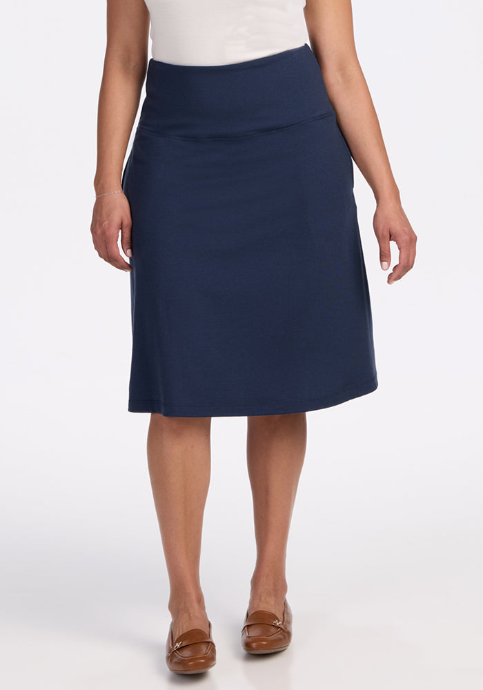 A person stands facing forward in a white top and the Woolx Marilyn Flowy Midi Skirt in Deep Navy, paired with brown flats. The background is plain white. | Kisha is 5'8", wearing a size M