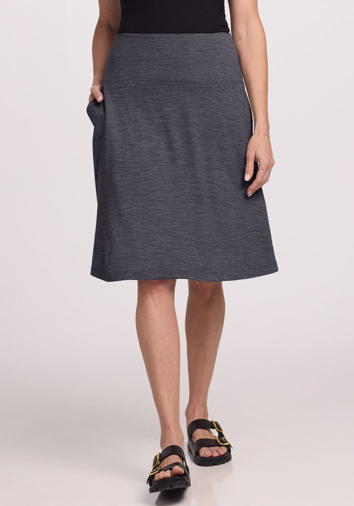 A person wearing the Woolx Marilyn Flowy Midi Skirt in Cinder Melange, paired with a black top and black sandals with gold accents, stands against a plain light background.