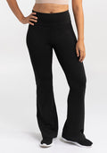 A person wearing Woolx's Marissa Pants - Black and black sneakers stands with one hand on their hip. The high-waisted pants are complemented by a cropped top that reveals their midriff, set against a plain, light background.