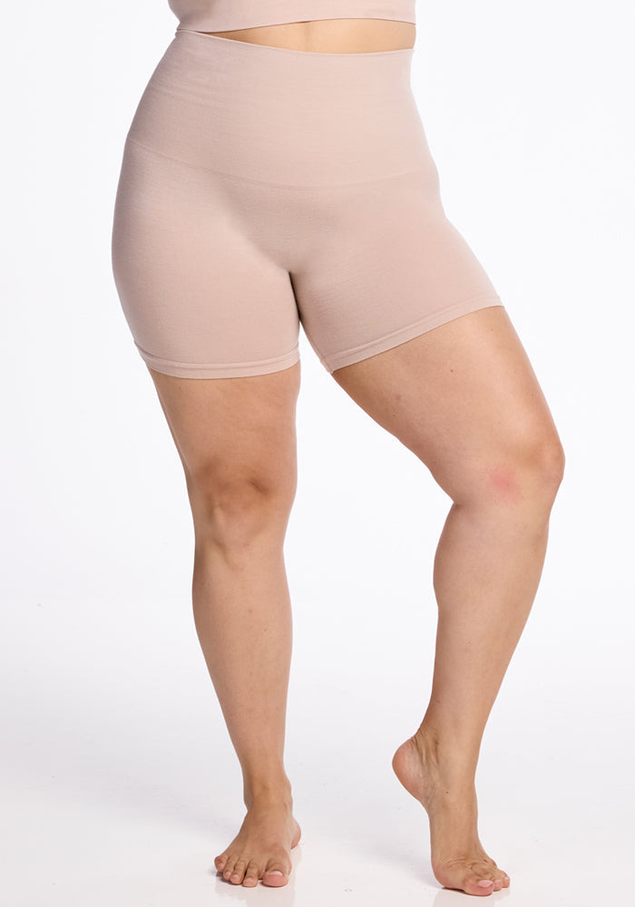 A person models the Woolx Marley Shapewear Shorts in Sand, featuring high-waisted, seamless compression design. Against a white background, they stand with one knee bent as the shorts fit snugly around their waist and thighs for perfect sculpting.