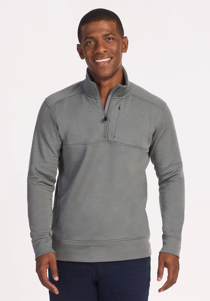 A man stands facing the camera, smiling with his hands by his sides, wearing the Woolx Mason 1/4 Zip in Sedona Sage—a men's wool pullover sweater with a chest pocket—against a plain white background.