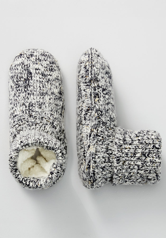 The Woolx Men's Gripper Slipper Bootie in Speckled Stone features cozy knit fabric with a fuzzy Sherpa lining; one bootie stands upright while the other is on its side, revealing the plush interior.