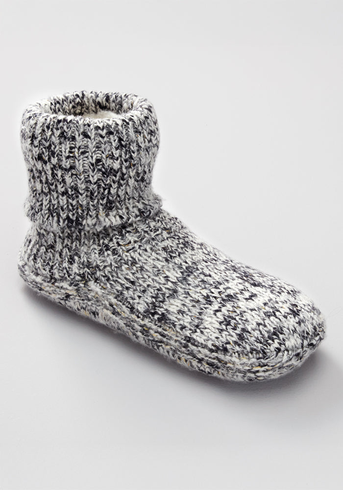 The Woolx Men's Gripper Slipper Bootie in Speckled Stone is a single gray and white Merino wool sock with a thick knit, Sherpa lining, ribbed ankle cuff, and grippers, shown on a plain light background.
