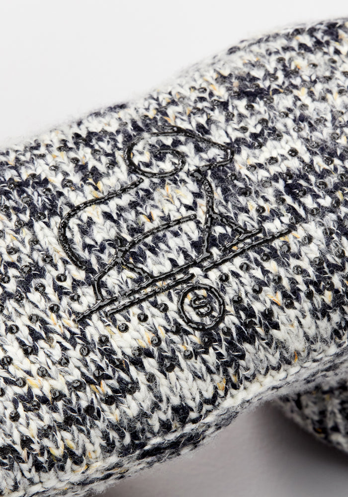 Close-up of the Men's Gripper Slipper Bootie - Speckled Stone by Woolx, featuring speckled black, white, and gray knit—ideal for lounging—and a simple black embroidered dog-on-skateboard design.