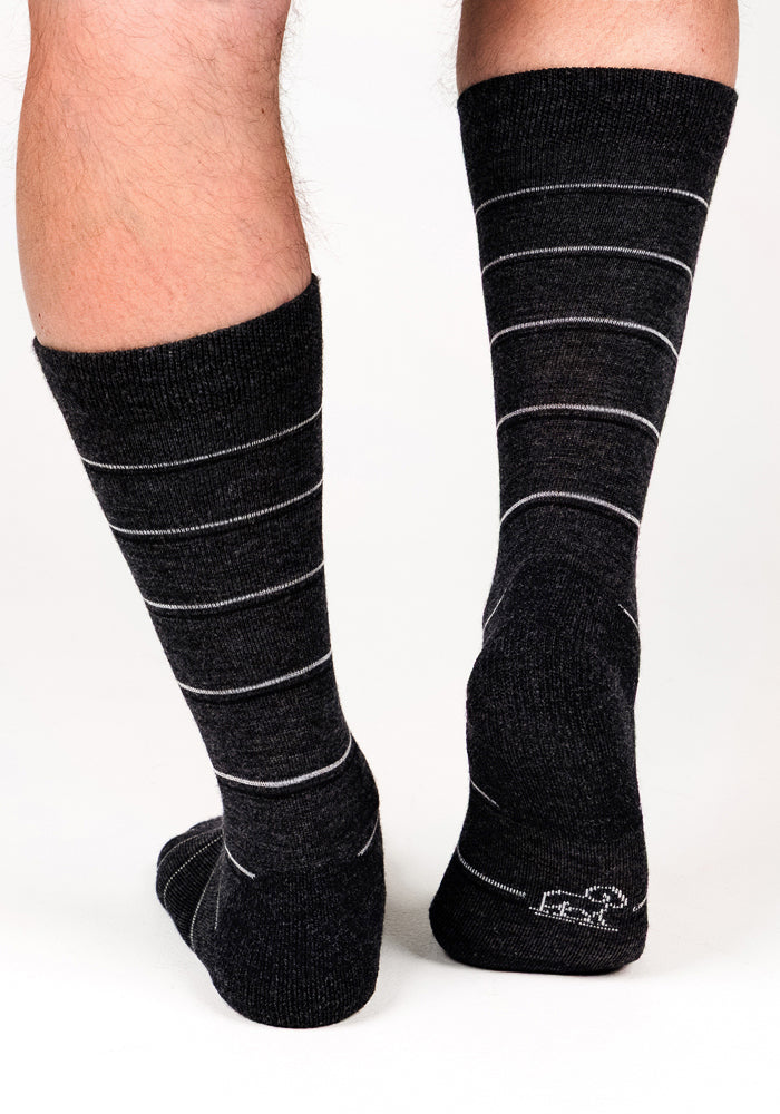 A close-up of a person's lower legs wearing Woolx Mens Chandler Mid Calf Socks in dark grey charcoal, standing on a white background.