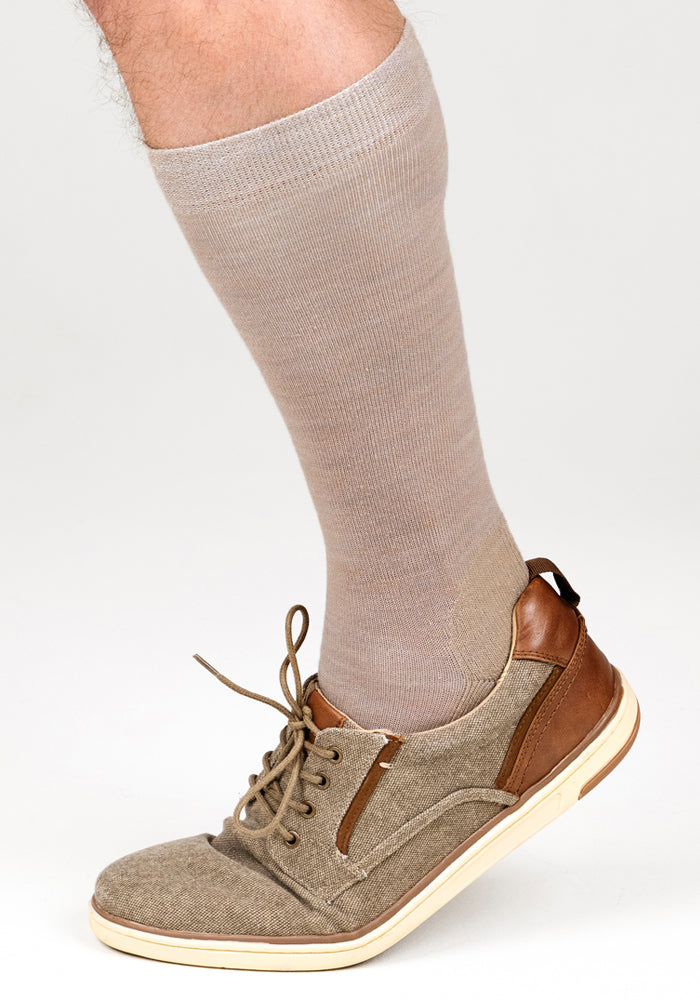 A foot wears Woolx Mens Chandler Mid Calf Socks in Simply Taupe with a tan lace-up shoe with brown accents, standing on tiptoe against a light background.