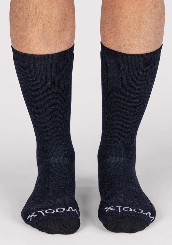 A person wearing Woolx Mens Core Crew Sock in navy stands on a light surface. "WOOL" is printed in white on the toes, and only the lower legs and feet are visible.