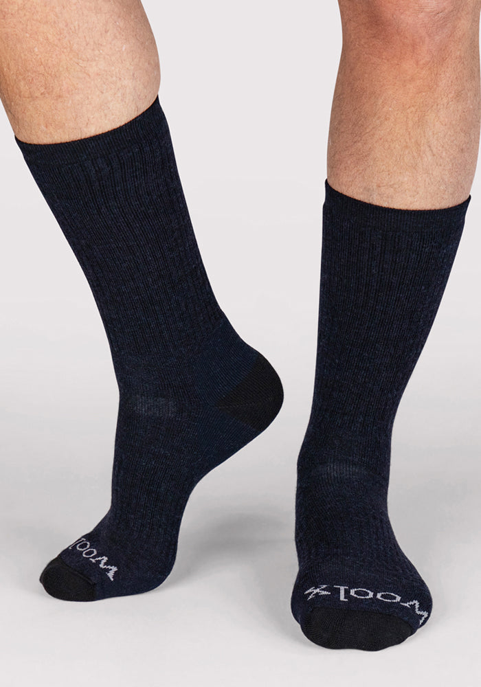 A person wears Woolx Men's Core Crew Socks in navy with black toes and "WOOLX" in white near the toes, against a light gray background.