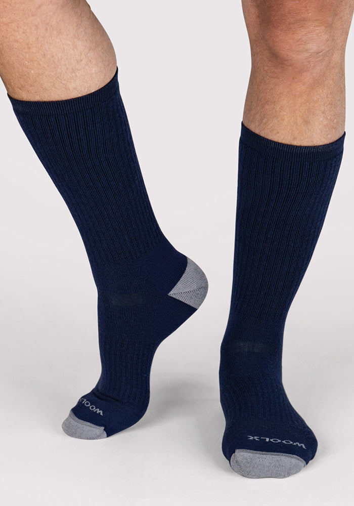 A person stands on a light background wearing Woolx Mens Core Crew Socks in Deep Navy with gray toes and heels. "WOOLX" is written near the toes.
