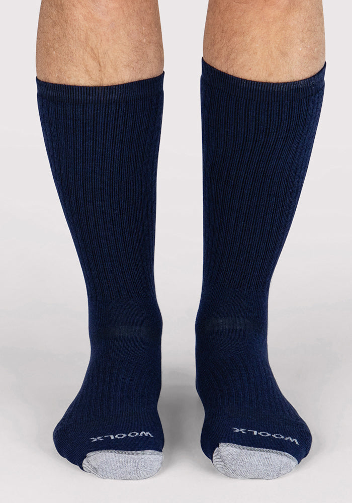 A pair of legs wears Woolx Mens Core Crew Socks in Deep Navy with light gray toes and "Woolx" printed in white. Moisture-wicking and cushioned, these socks deliver comfort for any adventure against a white background.
