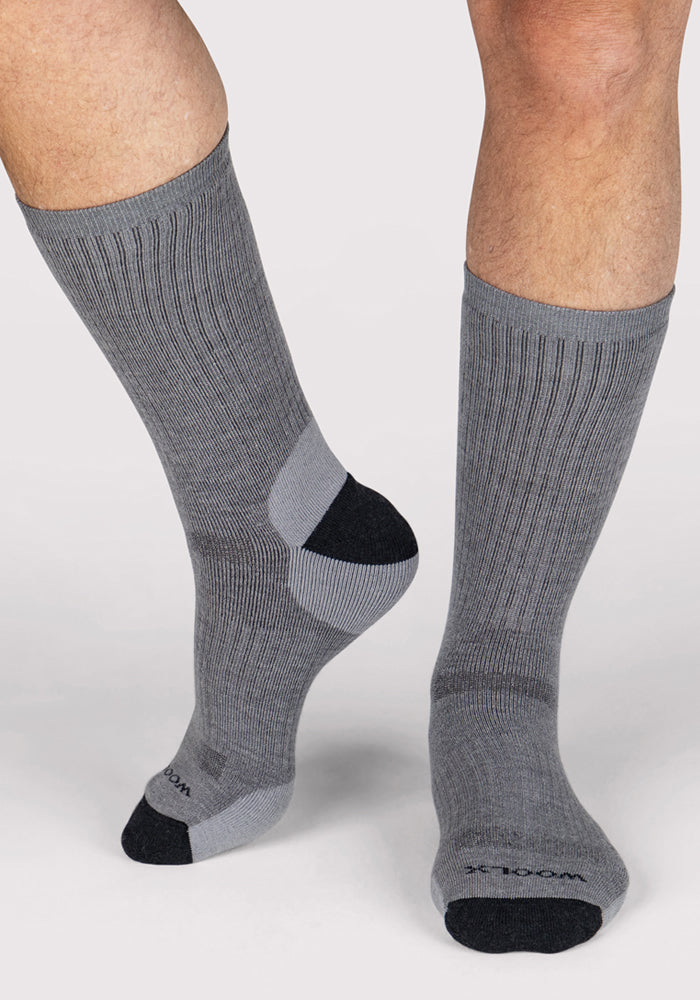 A person stands on a white background wearing Woolx Mens Core Crew Socks in grey, featuring black toes and heels; one foot is flat while the other is slightly raised.