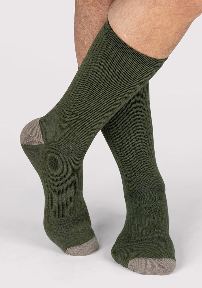 A person wearing Woolx Mens Core Crew Socks in Winter Moss with contrasting light gray heels and toes stands on a white background.