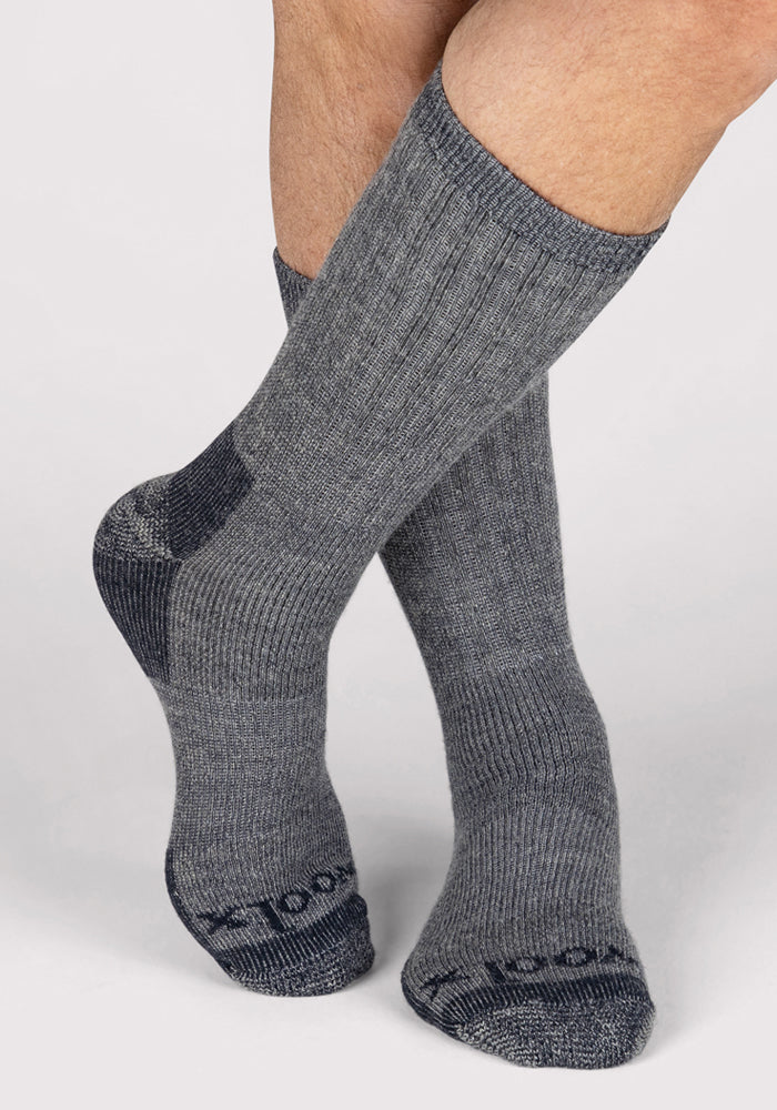 A pair of feet in Woolx Mens Extreme Crew Socks - Charcoal Heather, featuring thick ribbed fabric with darker heels and toes. Ankles are crossed against a light backdrop—ideal for staying warm in cold weather.