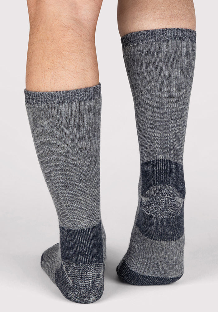 A close-up of a person's lower legs wearing Woolx Mens Extreme Crew Socks in Charcoal Heather with darker gray heels, toes, and cuffs on a light background—ideal winter socks for men in cold weather.