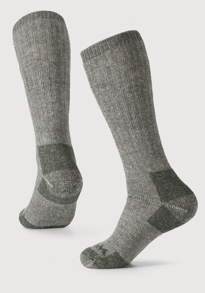 The "Extreme Extra Cushion Over The Calf - Forest Dark Moss" from Woolx are showcased on an off-white background. Made from Merino wool fabric, these dark green cold-weather socks boast a ribbed texture with reinforced heels, toes, and arches in a darker shade for superior insulation.