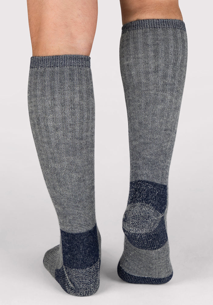A pair of legs wearing Woolx Mens Extreme Over The Calf Socks in Navy Carbon, featuring darker heels, toes, and soles, shown from the back against a plain light background.
