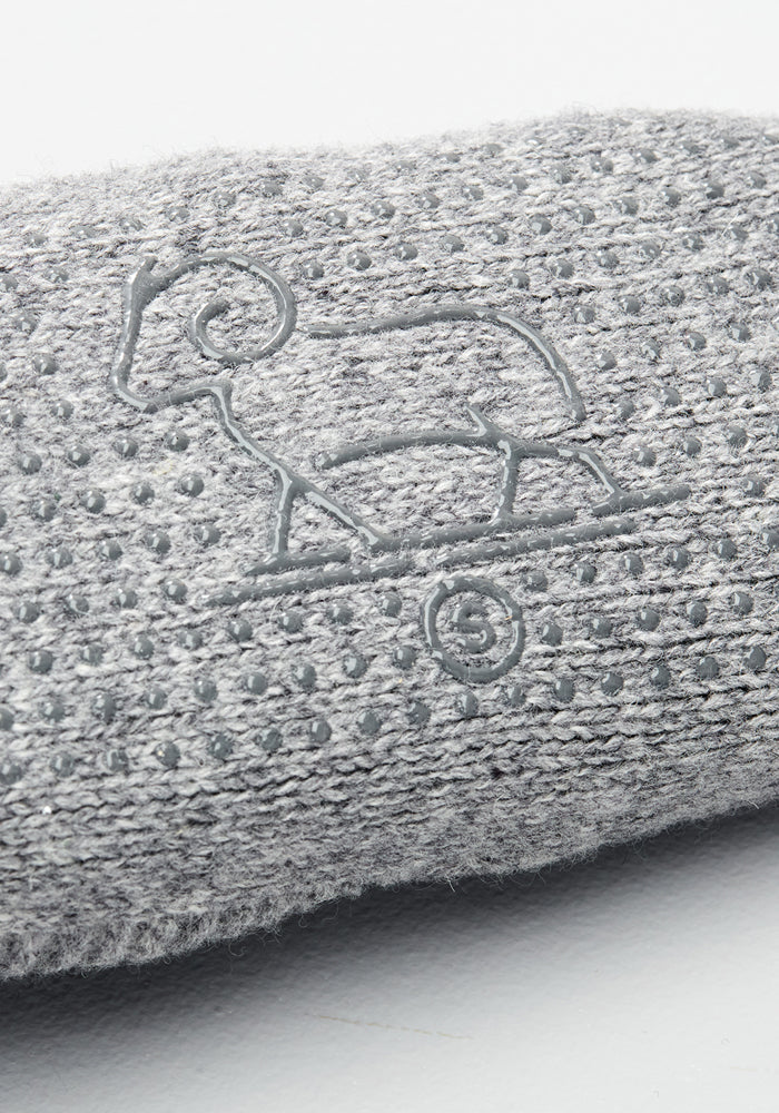 Close-up of Woolx Mens Gripper Slippers in Gentle Grey, showing the textured fabric with raised grip dots and an embroidered ram outline standing on a spiral design.