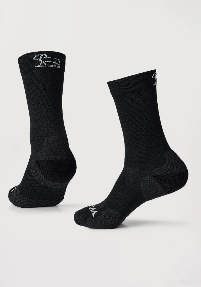 The Woolx Harbor Crew Sock Light Cushion in black features a white embroidered rabbit logo near the top. Displayed on a plain white background, one sock stands upright while the other is angled to highlight heel and sole details.