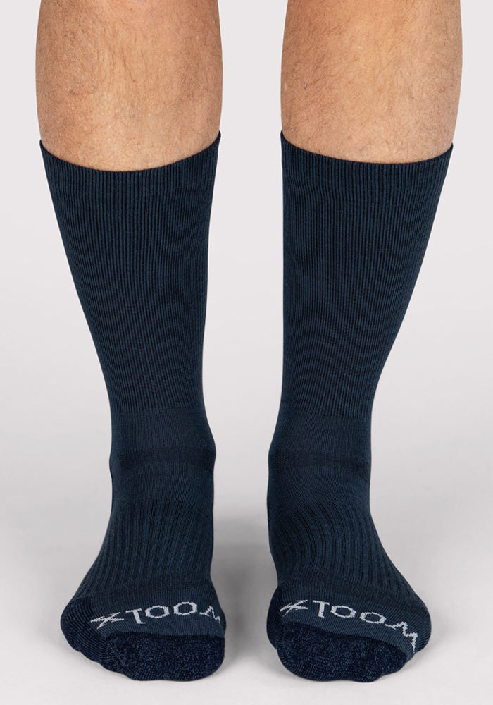 A pair of feet wearing Woolx Mens Harbor Crew Sock - Evening Tide, featuring moisture-wicking fabric and "XTOOL" in white on the toes, stand on a light gray surface.