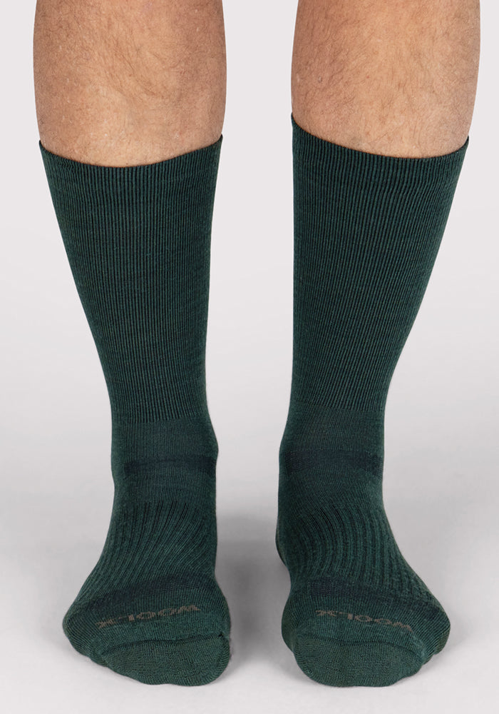 A pair of adult legs wearing Woolx Mens Harbor Crew Sock - Forest, moisture-wicking and breathable, standing on a white background.