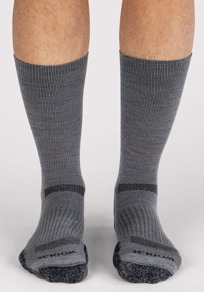 A pair of feet in Woolx Mens Harbor Crew Socks - Grey, featuring breathable fabric, darker gray toes and heels, plus horizontal stripes across the midfoot, standing on a light background.