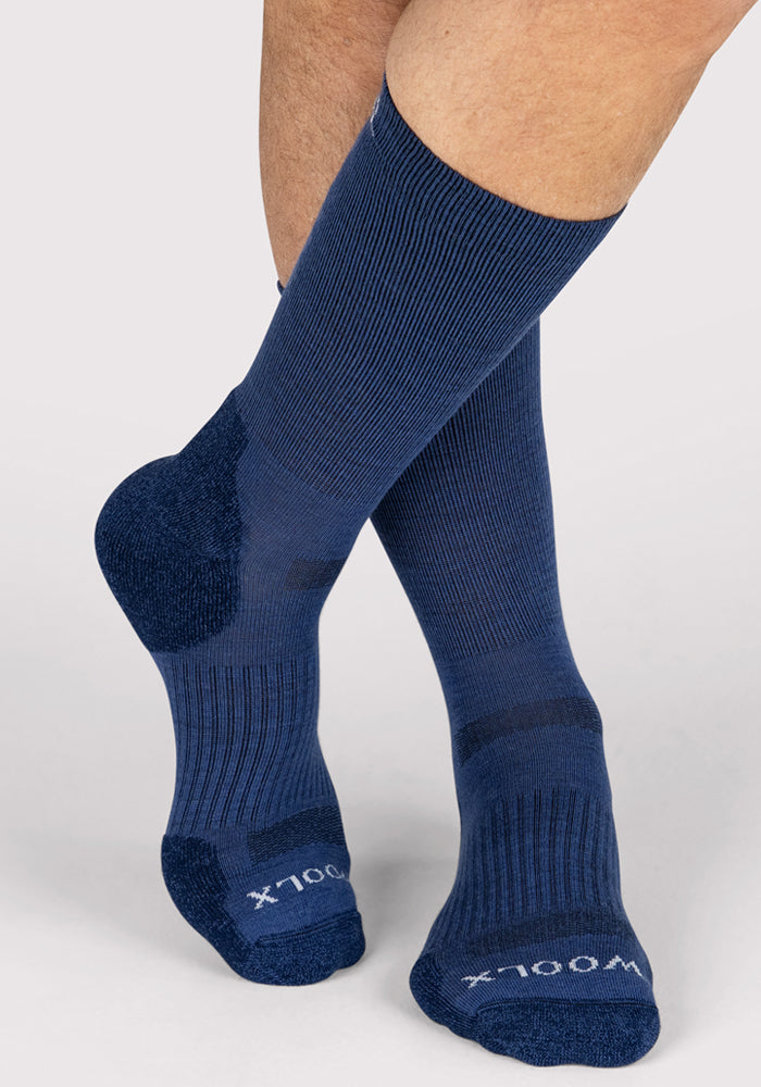 A close-up of a person wearing Woolx Mens Harbor Crew Sock in Sailor Blue, featuring ribbed texture and darker reinforced heel, toe, and sole areas for enhanced durability and comfort, with one leg crossed over the other.
