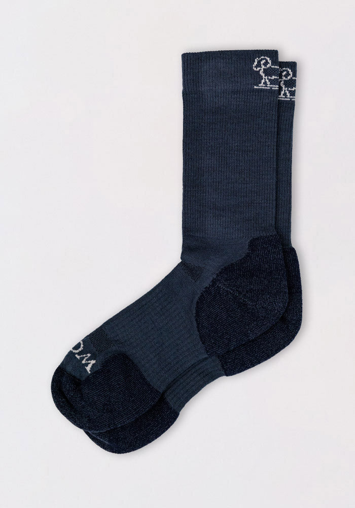 The Woolx Mens Harbor Crew Sock in Evening Tide is a dark blue, moisture-wicking sock with a light blue foot section and small white stick figure embroidery on the cuff, shown laid flat on a light background.