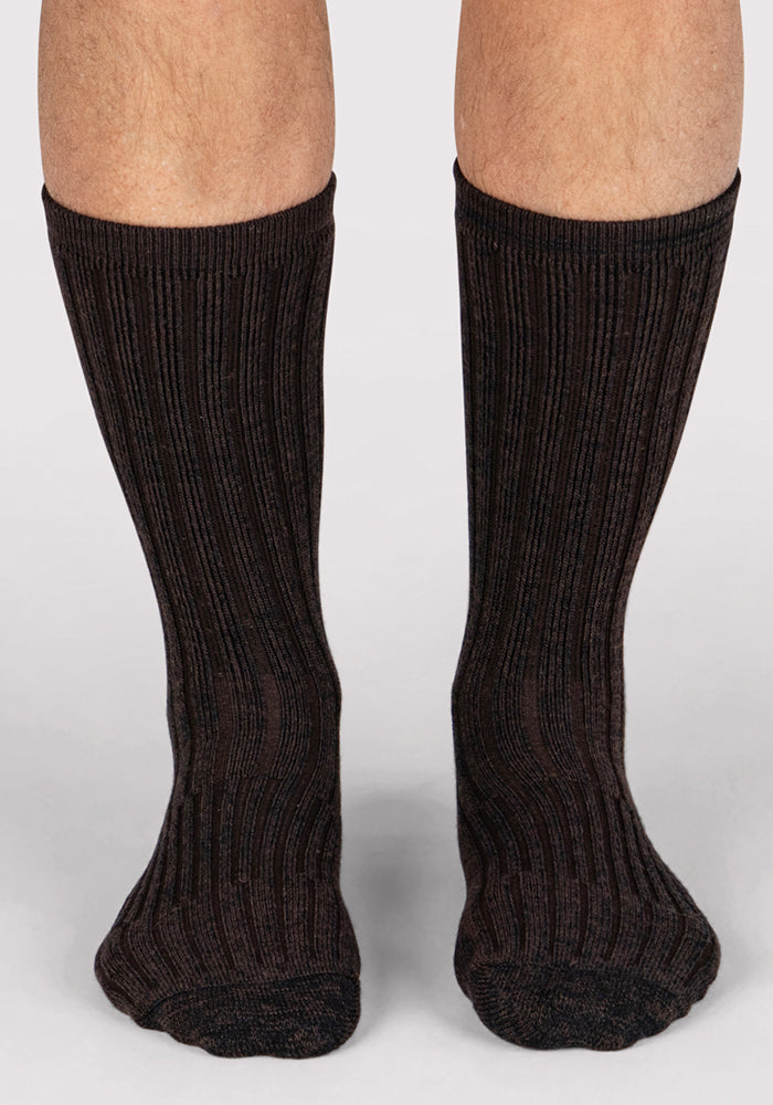 A close-up of a person's lower legs wearing Woolx Mens Joey Crew Socks in Dark Espresso, standing on a neutral background.
