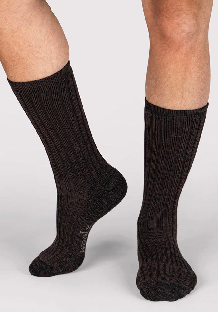 A person wearing Woolx Mens Joey Crew Socks in Dark Espresso stands on a light surface. The ribbed crew socks feature a subtle pattern and provide mid-calf coverage. Only the lower legs and feet are shown.