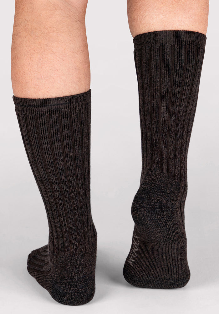 A close-up of two legs wearing Woolx Mens Joey Crew Socks in Dark Espresso, ribbed and mid-calf length, standing on a light background.