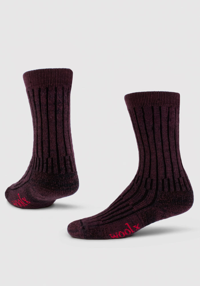 A pair of cozy Woolx Mens Joey Crew Socks in Warm Violet with vertical black stripes and "woolx" in pink on the toe, made from soft merino wool, shown against a light gray background.