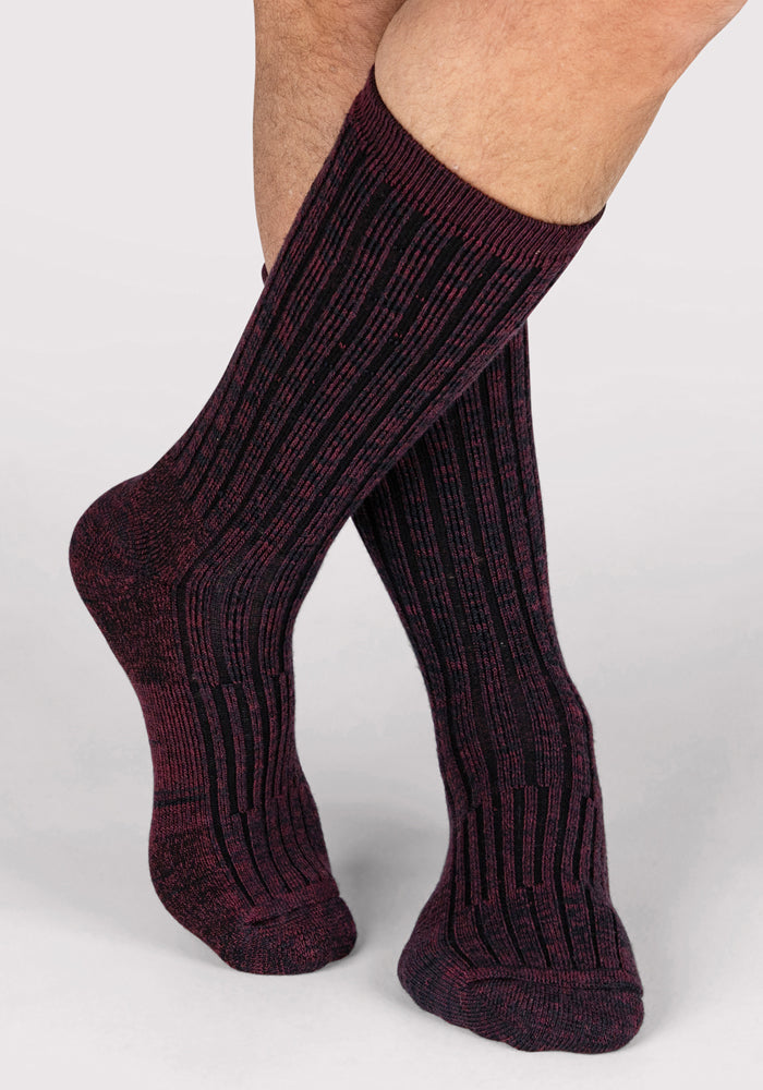 A person wearing Woolx Mens Joey Crew Socks in Warm Violet stands with their legs crossed against a plain light background.