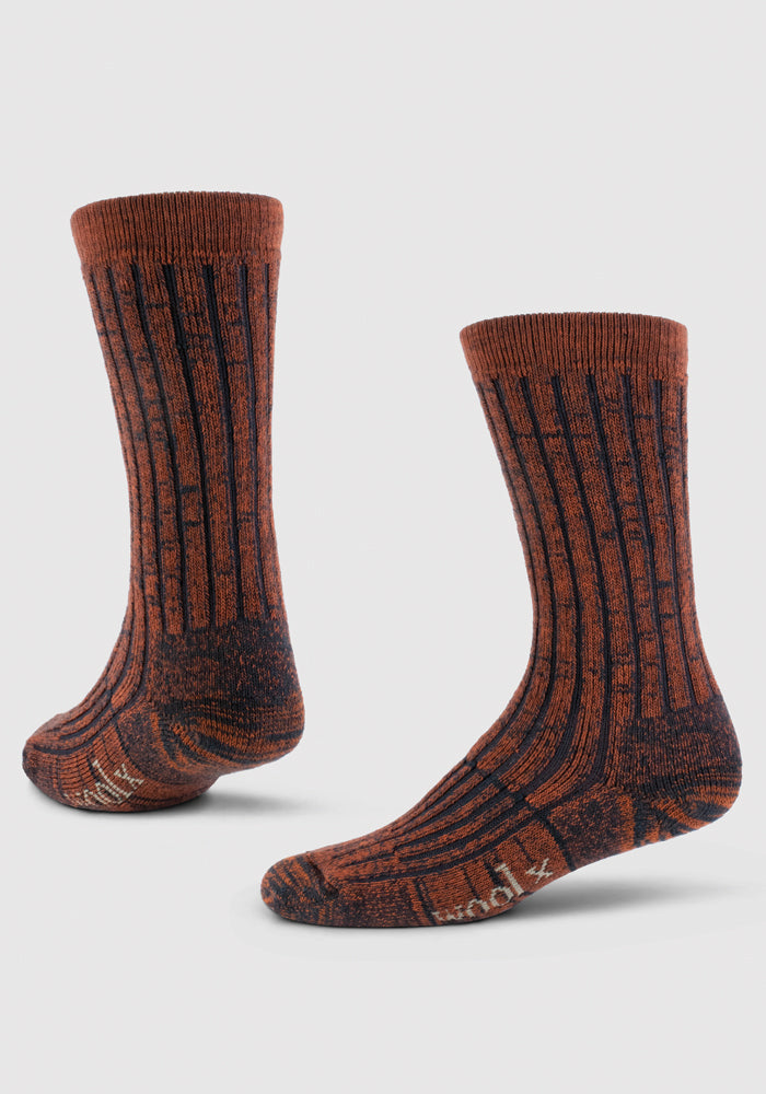 A pair of Joey Full Cushion Mid Calf Socks in Cinnamon Spice from Woolx stands upright on a light gray background, showcasing their textured, speckled brown and black design with ribbed detailing. The socks feature a cushioned sole with the brand name visible near the toe.