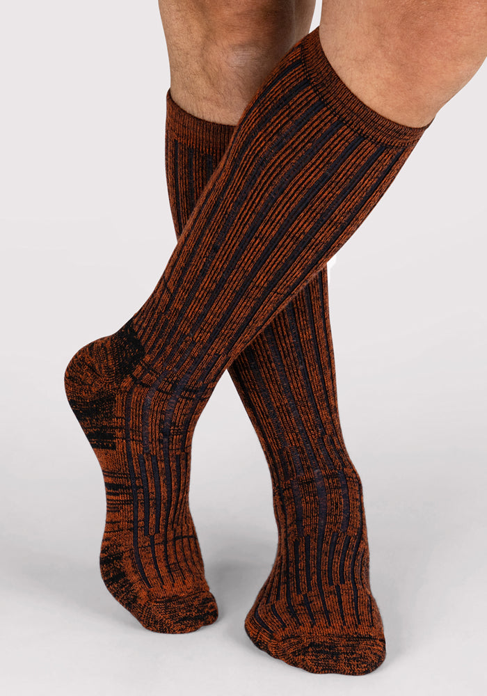A person stands with one leg crossed in front of the other against a plain light background, wearing Woolx Mens Joey Mid Calf Socks in Cinnamon Spice.