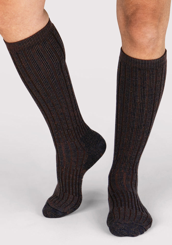 A person wears Woolx Mens Joey Mid Calf Socks in Dark Espresso, standing on a light background.