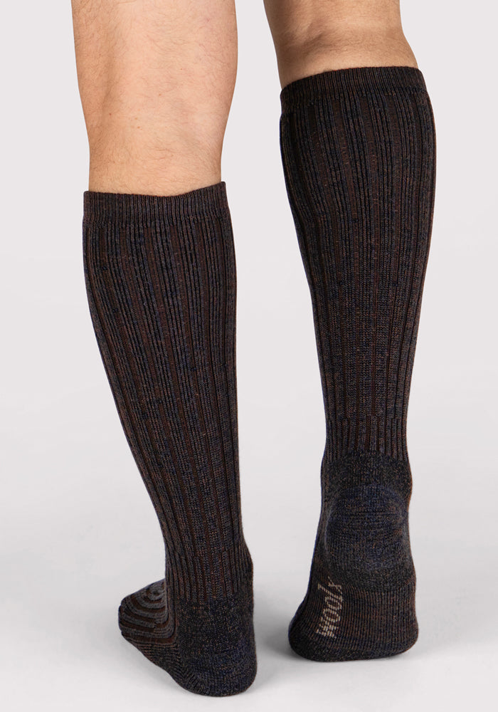 A person is wearing Woolx Mens Joey Mid Calf Socks in Dark Espresso, standing on a light surface with the back of their legs visible.