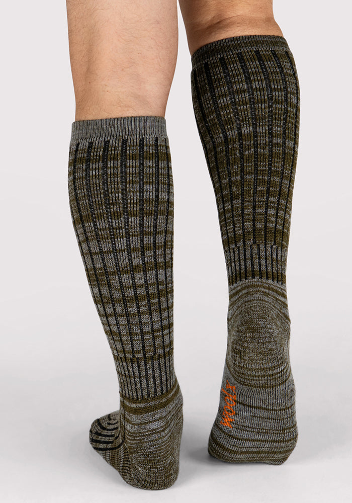 A close-up of a person from the knees down wearing Woolx Mens Joey Mid Calf Socks in Dark Forest Marled, featuring reinforced heels and toes for lasting comfort, standing on a light background.