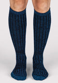 A person stands on a light gray surface wearing Woolx Mens Joey Mid Calf Socks in Steel Blue, featuring a ribbed design with blue and black vertical stripes.