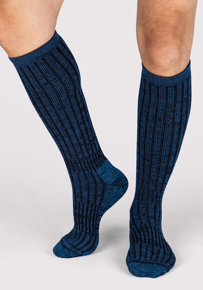 A person wearing Woolx Mens Joey Mid Calf Socks in Steel Blue stands on a light gray background.