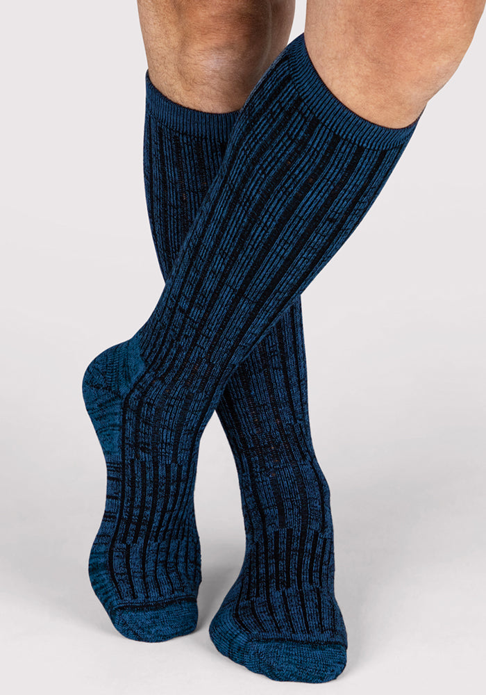 A person stands with legs crossed at the ankles against a plain light background, wearing Woolx Mens Joey Mid Calf Socks in Steel Blue.