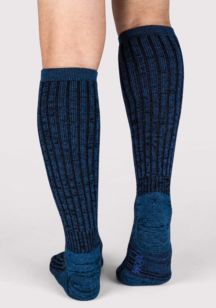 A person stands on a light gray background, showing the back view of Woolx Mens Joey Mid Calf Socks in Steel Blue.