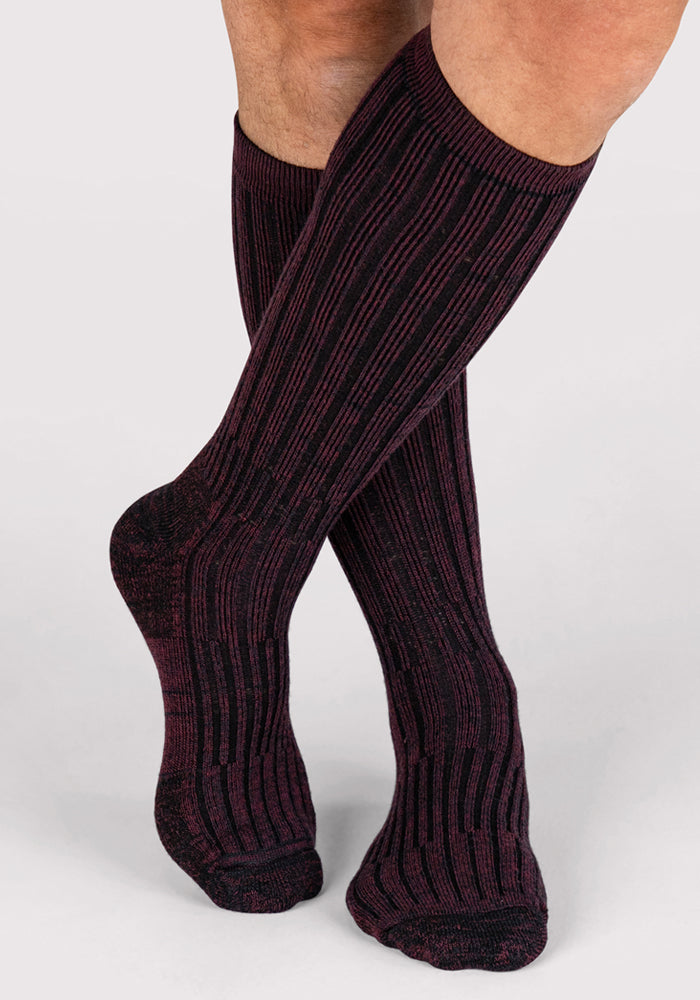 A person wearing Woolx Mens Joey Mid Calf Socks in Warm Violet stands with feet crossed on a light gray background.