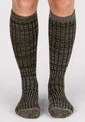 A person wearing Woolx Mens Joey Mid Calf Socks - Dark Forest Marled, featuring a ribbed texture in gray and olive green, stands on a plain light background.