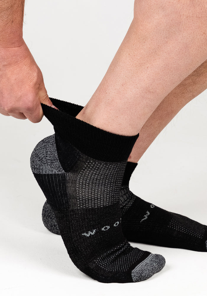 A person pulls on a Woolx Mens Rambler Ankle Sock in Black Pepper against a plain white background.