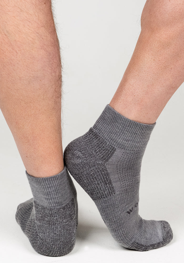 A close-up of two feet in Woolx Mens Rambler Ankle Sock - Pebble, positioned heel to heel against a plain white background, highlights the socks' exceptional moisture management.