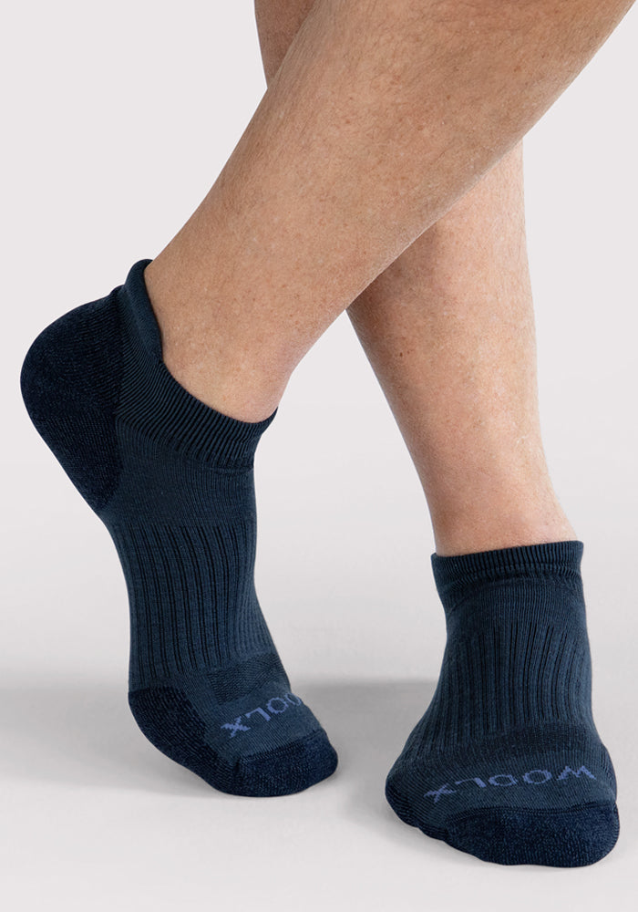 A man wearing Woolx Mens Rowan No Show Socks in Evening Tide stands with one leg crossed over the other against a plain light background.
