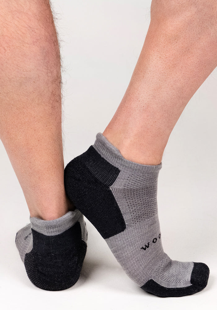 A pair of Woolx Mens Rowan No Show Socks - Pebble in gray and black, with a textured pattern and reinforced heel and toe, are arranged heel to heel on a plain white background. The socks feature moisture-wicking fabric for comfort.